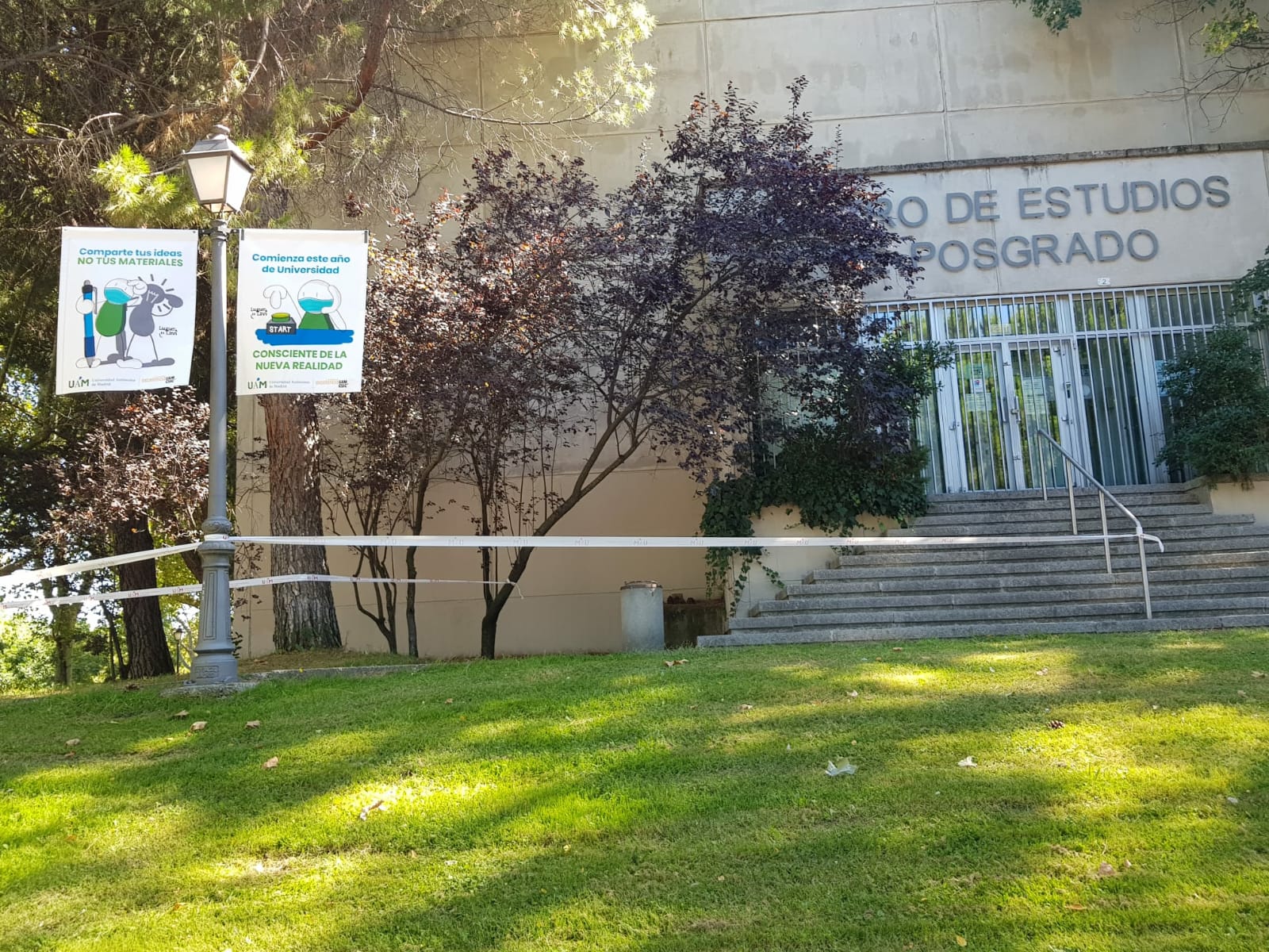 Imagen de la entrada principal del Edificio de Posgrado, con carteles de la campaña de medidas para prevenir la Covid-19
