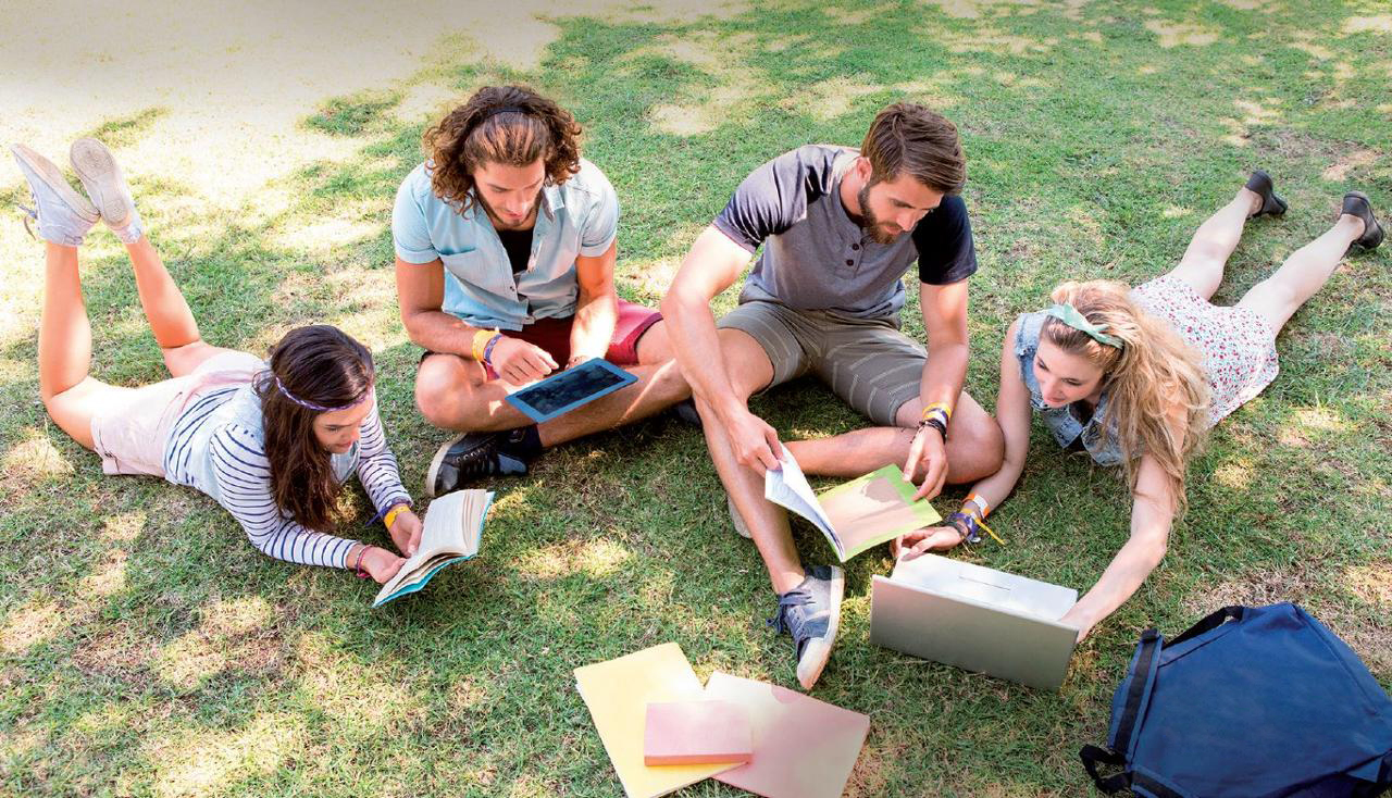 Varios estudiantes leen en grupo sobre el césped