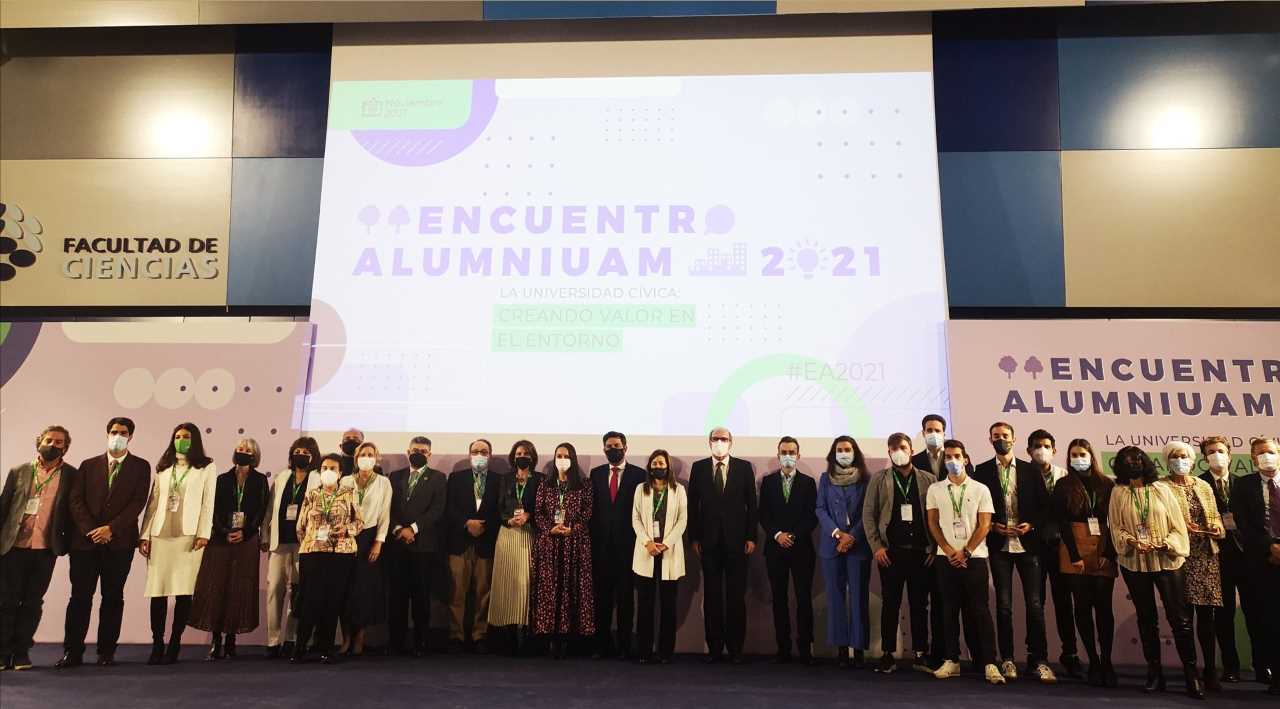 Foto de Grupo de los premiados en Premios AlumniUAM 2021 con el cartel del programa al fondo