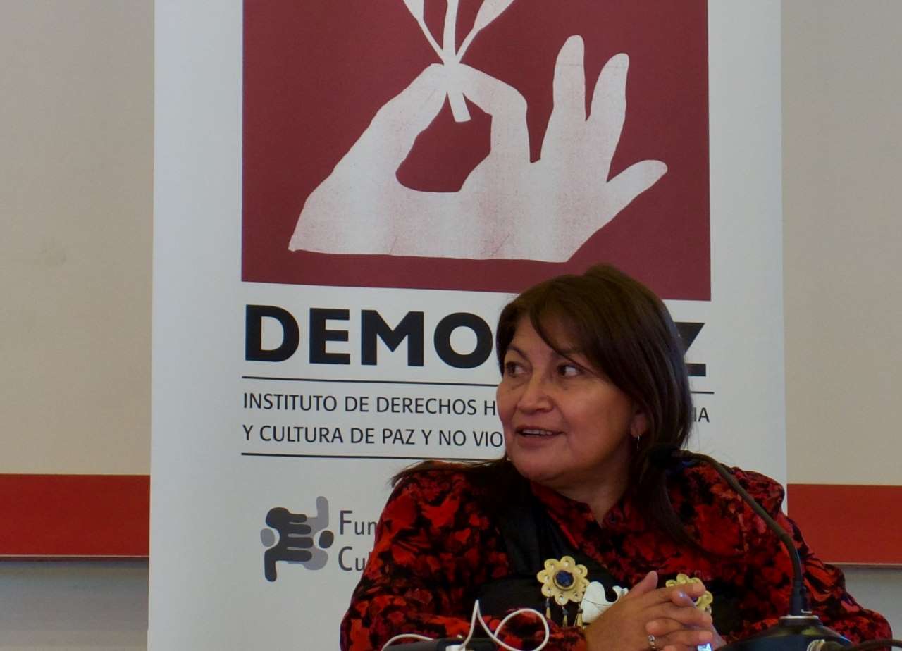 Primer plano de la académica y activista chilena Elisa Loncón con el logo de Demospaz detrás de ella