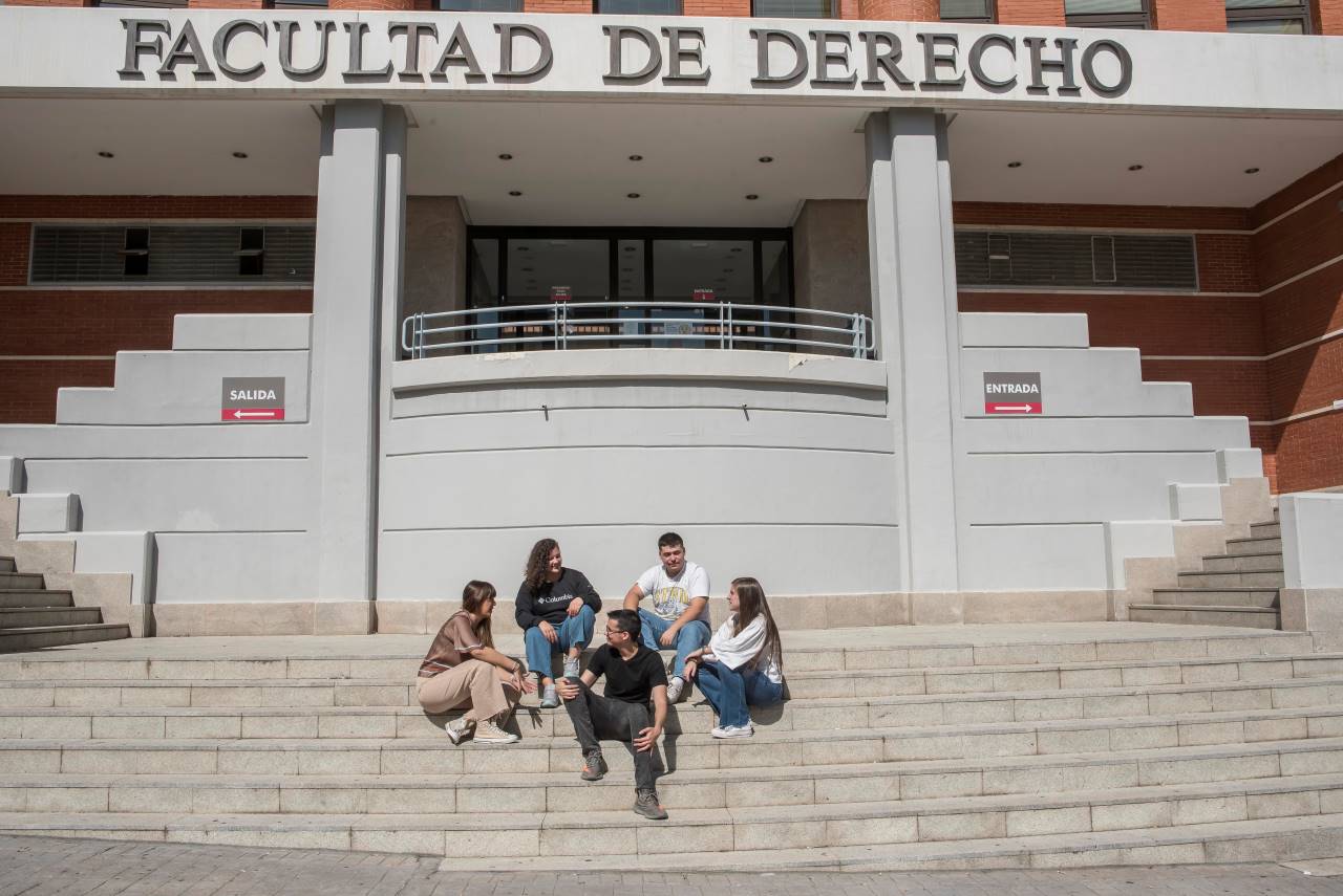 Varios estudiantes sentados en las escaleras de la entrada principal de la Facultad de Derecho