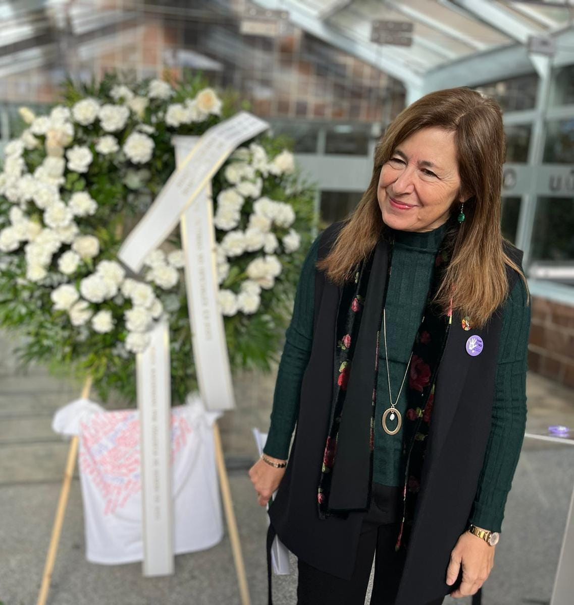 Imagen de la rectora junto a la corona de rosas y claves blancos en solidaridad con las víctimas y sus familias.