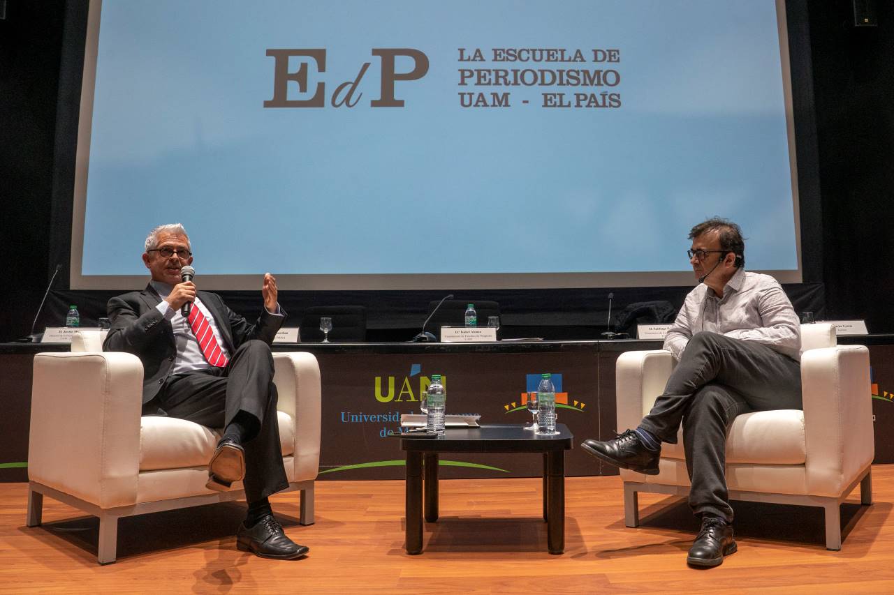 A la izquierda, el director de la Escuela UAM-El País, Javier Moreno, conversa con el escritor Javier Cercas. Al fondo, trasera blanca con letras negras en la que puede leerse Escuela UAM-El País 