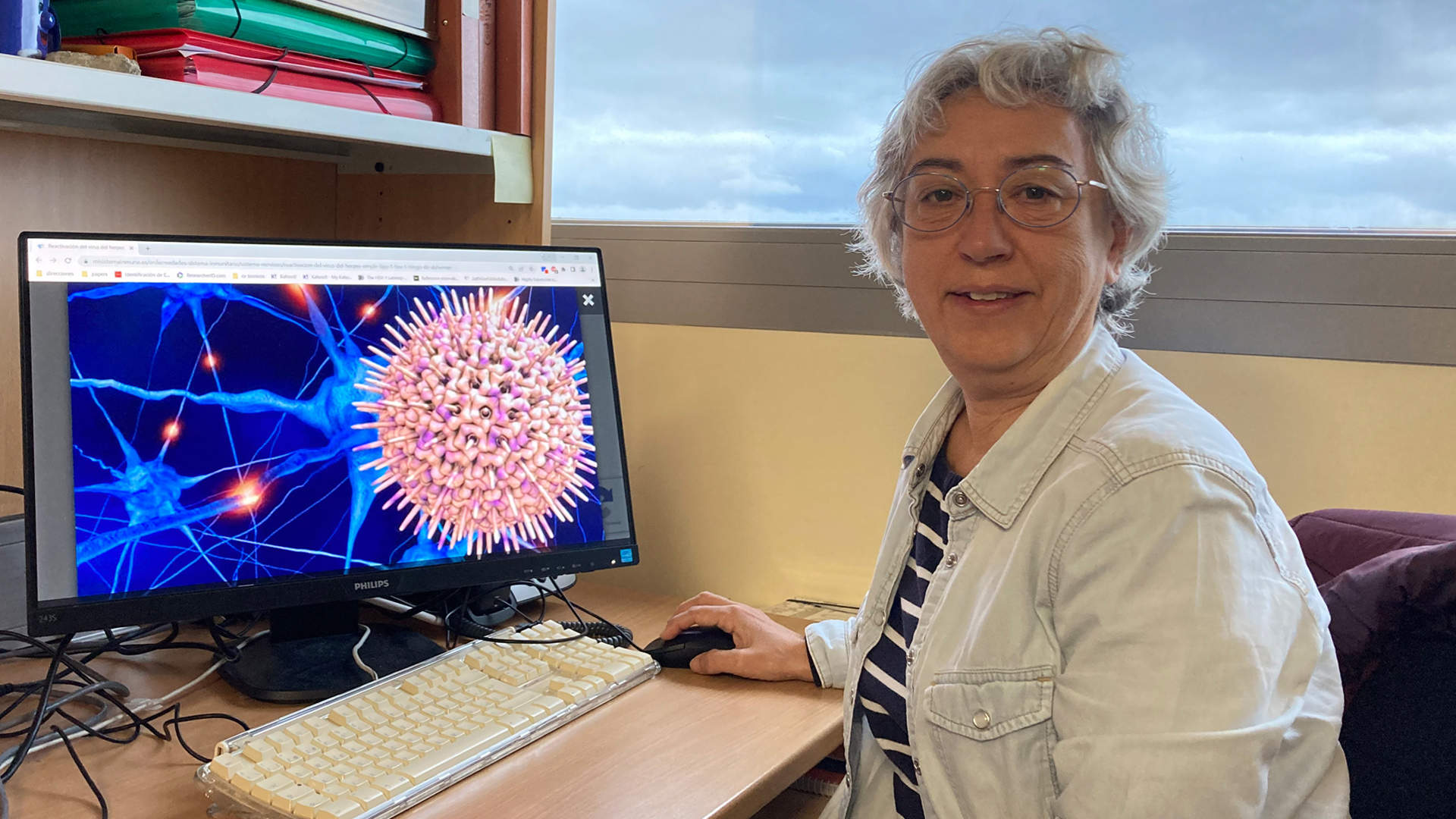 La doctora María Jesús Bullido en su despacho, junto a una imagen del virus del herpes