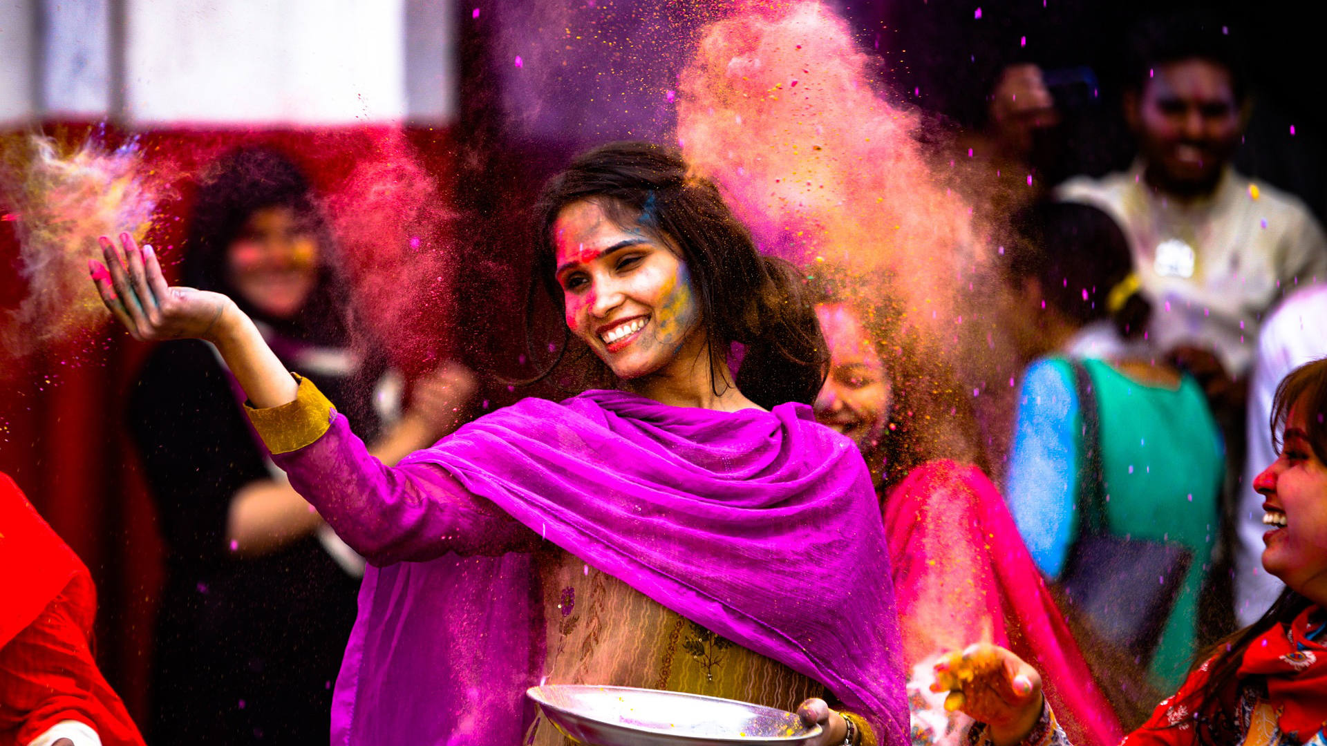 Imagen de una mujer india en fista de los colores sonriendo y lanzando pigmento.
