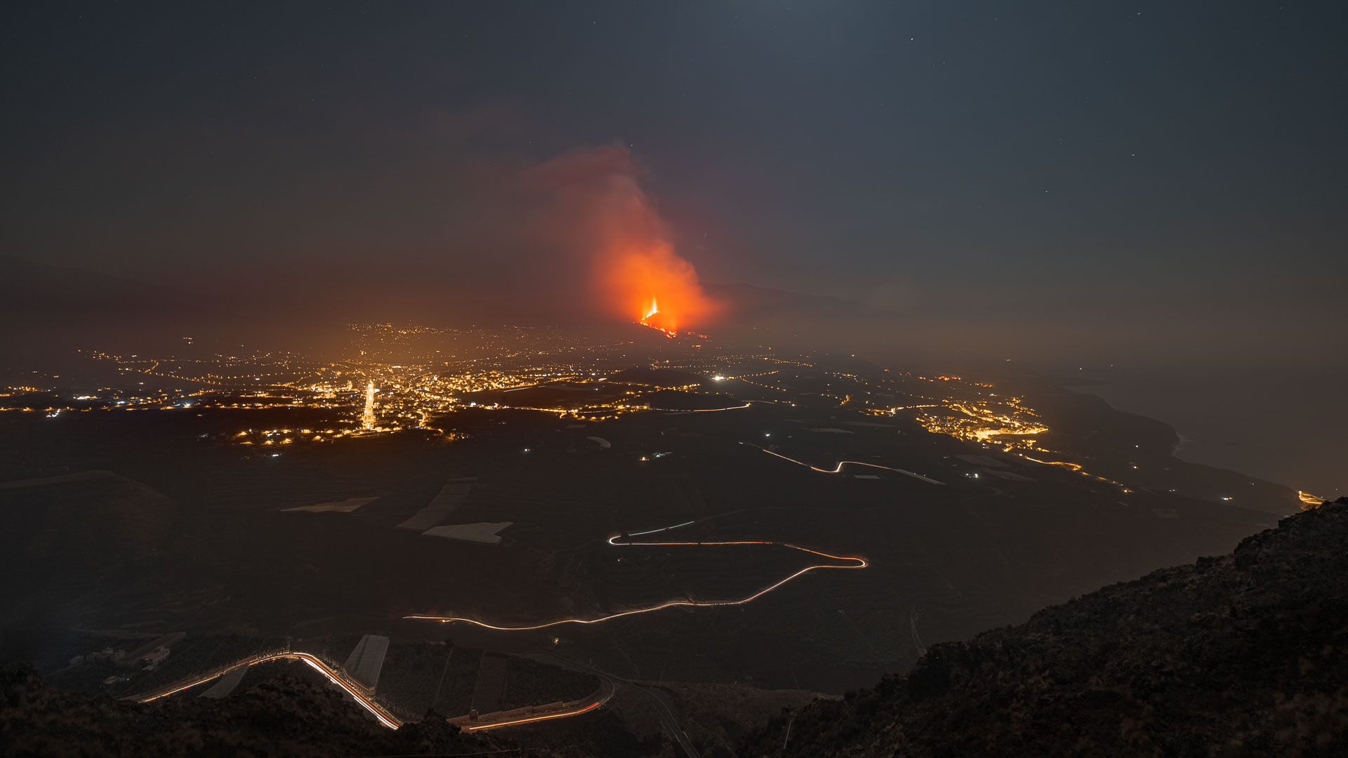 Imagen en la que aparece un volcán en erupción rodeado de las luces de carretera y ciudades cercanas
