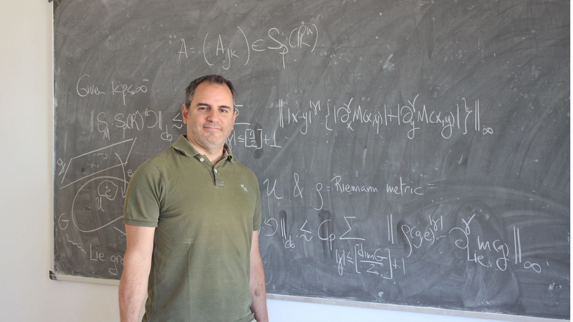 Fotografía del investigador delante de una pizarra tradicional con fórmulas matemáticas.
