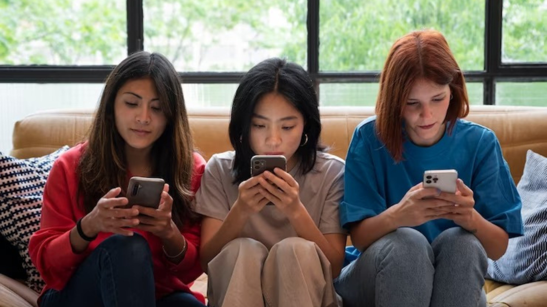 Tres adolescentes sentadas en un sofá con el móvil en la mano mirando sus pantallas.
