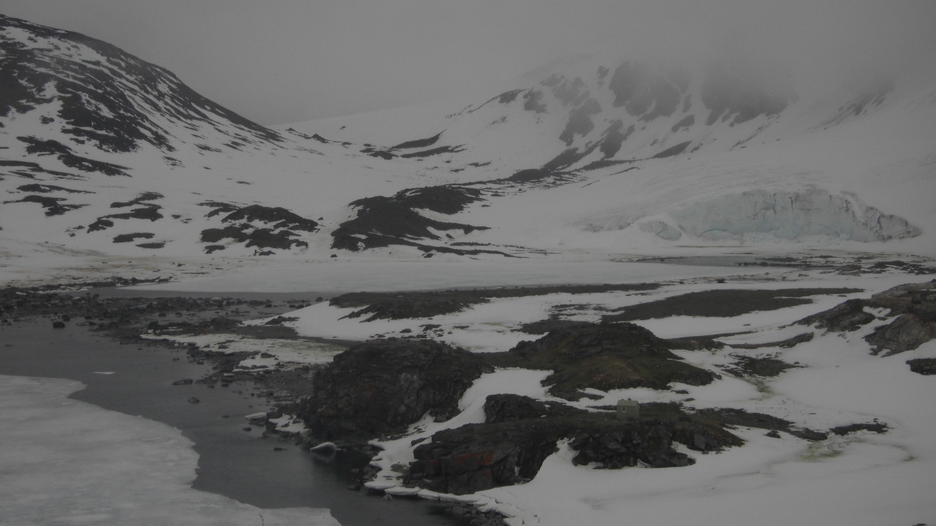 Fotografía de una ladera cubierta de hielo y la costa marina de color gris.