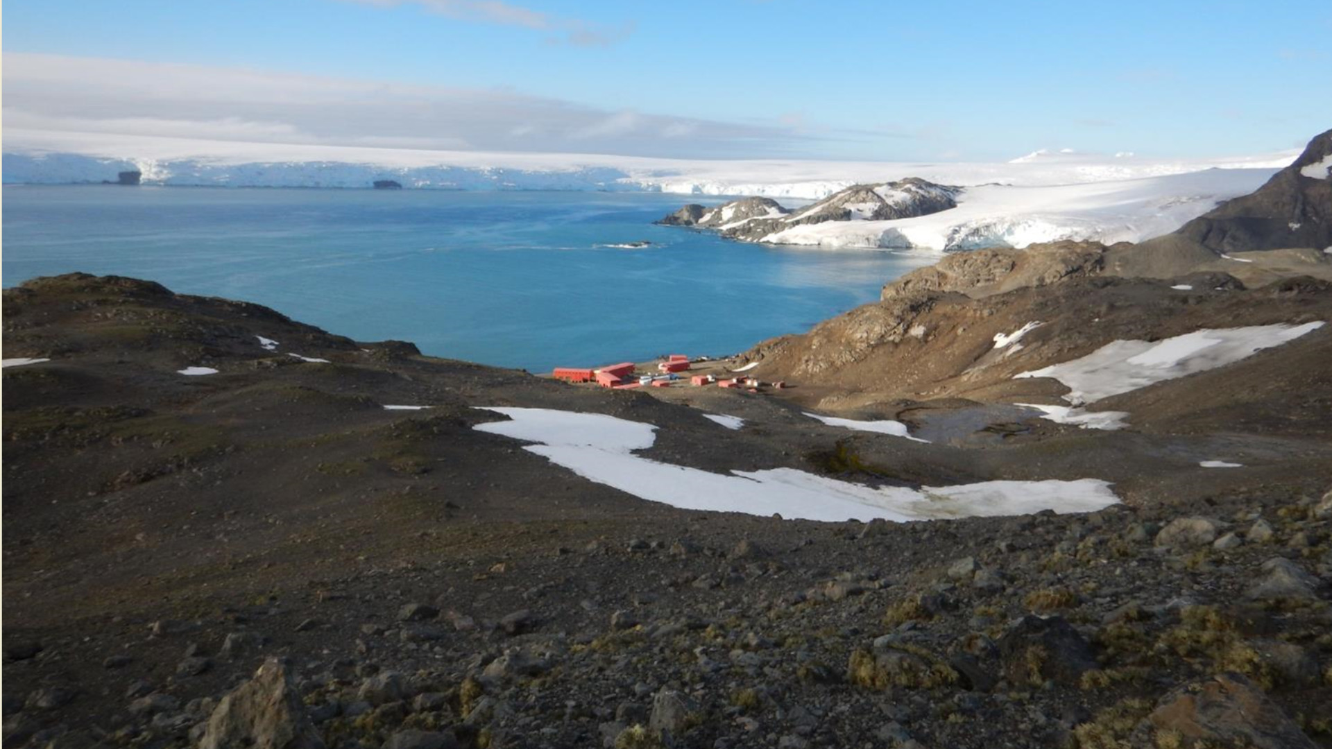 Fotografía de un paisaje natural donde aparece una edificación pequeña sobre un bahía parcialmente cubierta de hielo y cielo azul.