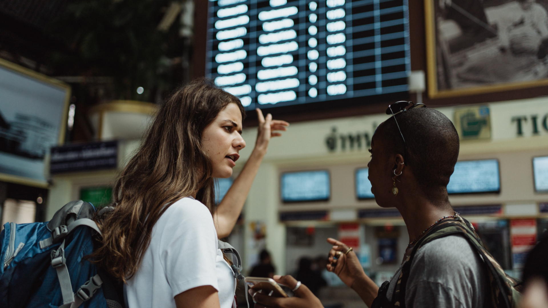Fotografía de dos mujeres en la sala de un aeropuerto mirando la tabla de salidas.