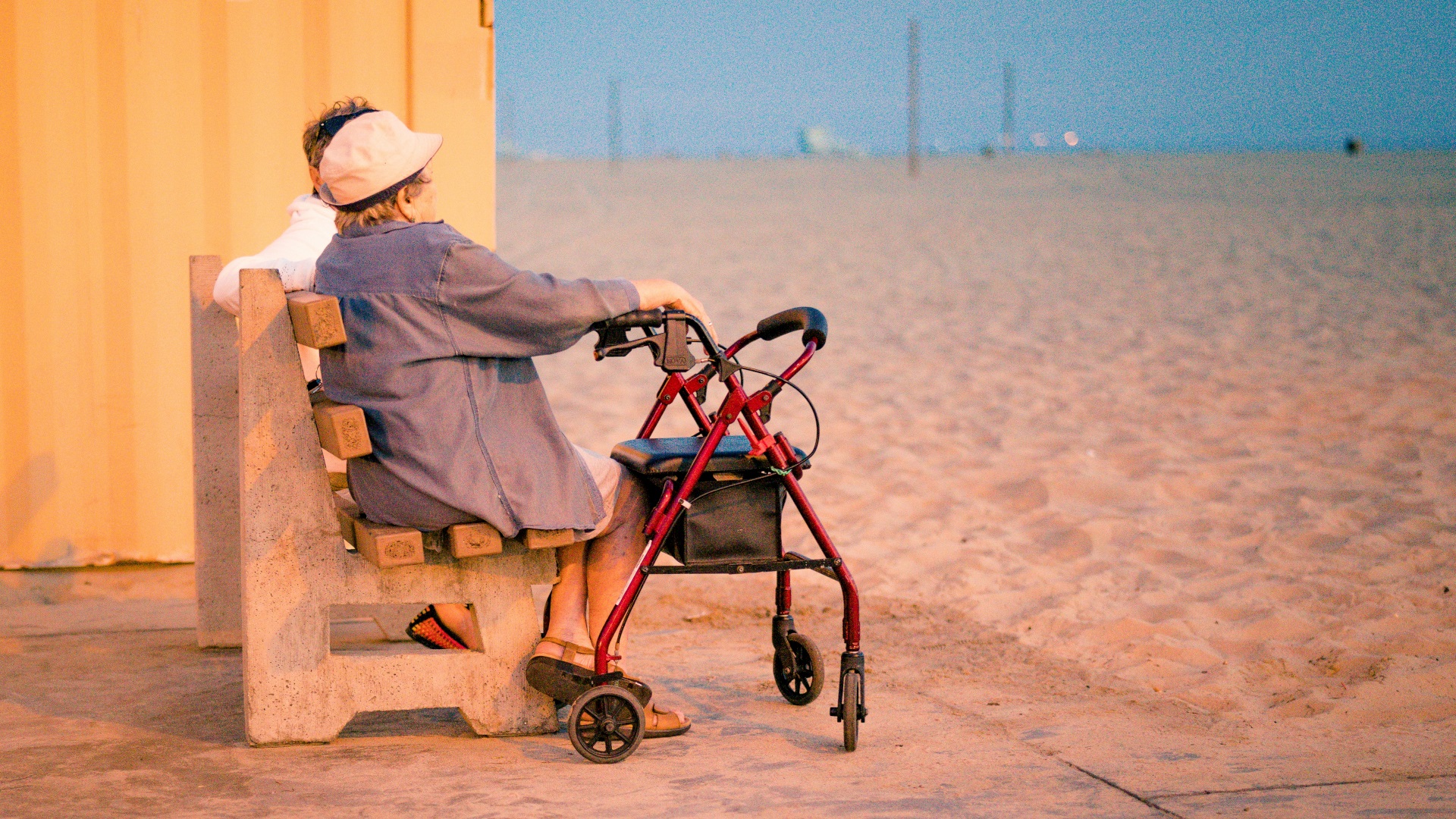 Fotografía de ancianos sentados en un banco mirando a la playa, en tonos ocres.