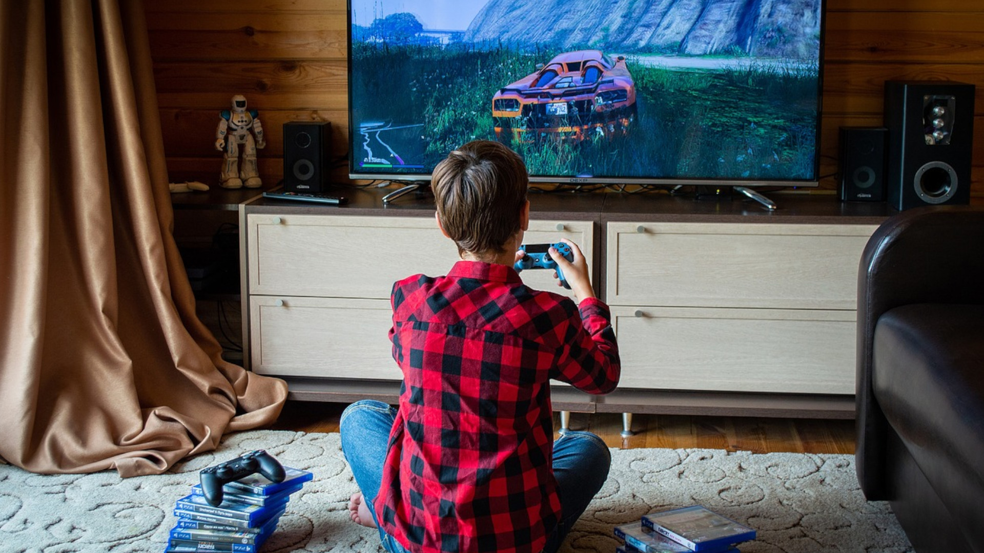 Fotografía de un jugador sentado en el suelo frente a la pantalla de televisión, con los mando en la mano.