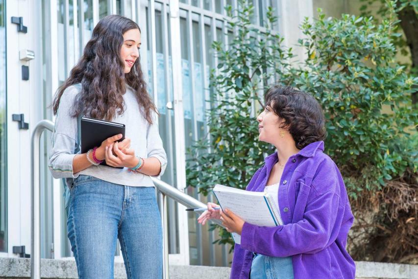 dos estudiantes conversan animadamente frente a su facultad