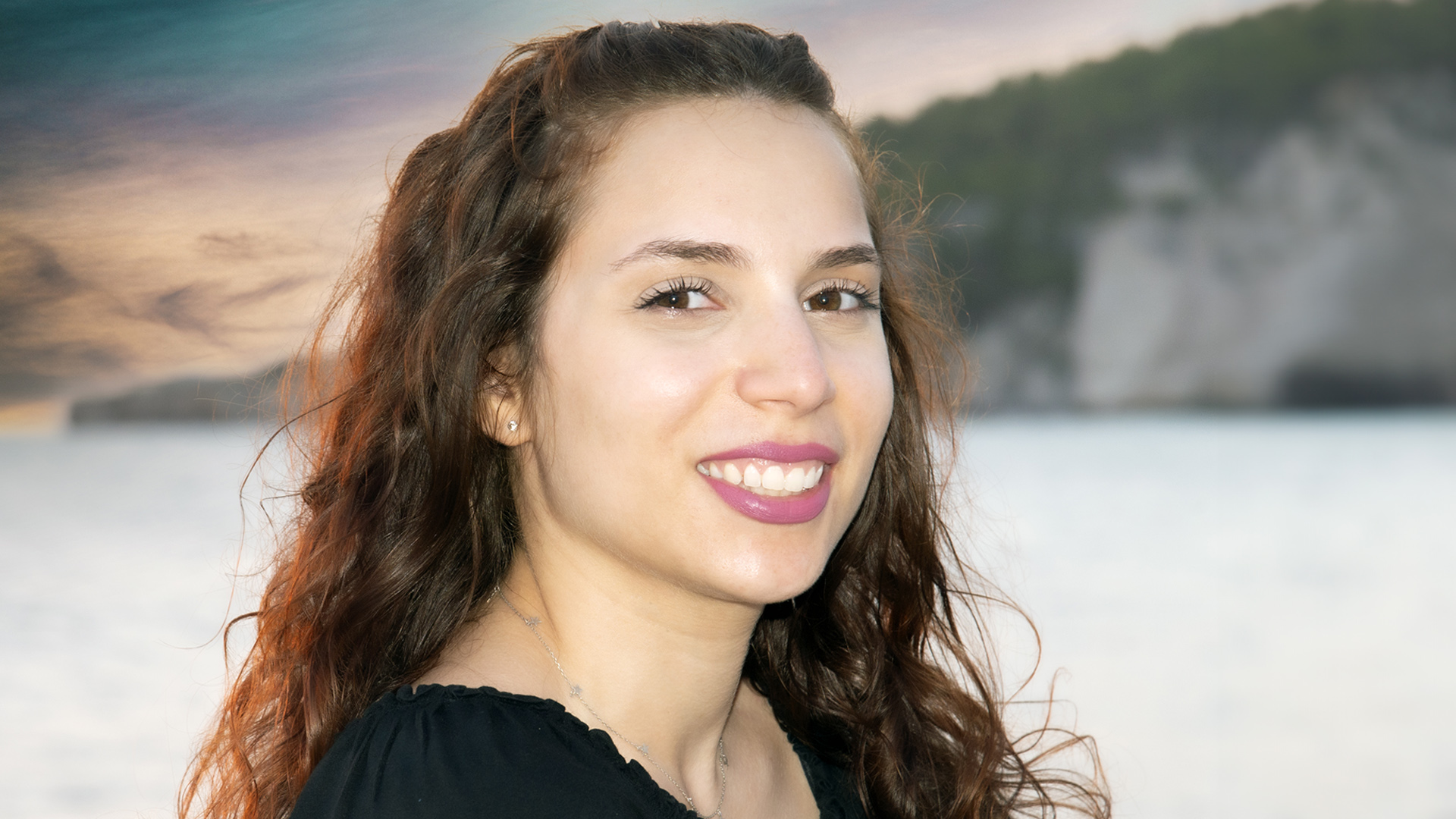 Fotografía de rostro de mujer sonriendo, con pelo largo rizado y fondo de mar.