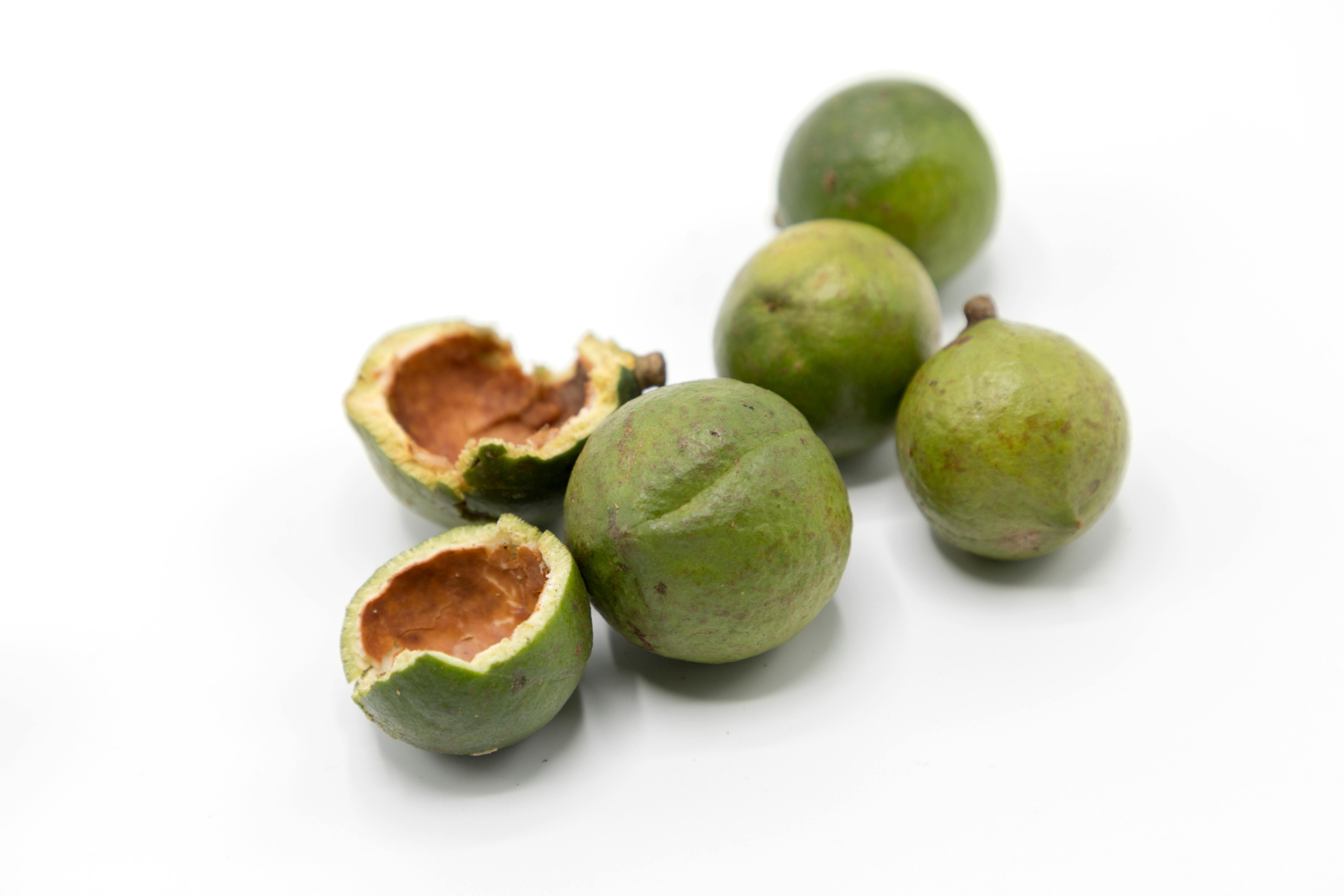 Fotografía de unas nueces de macadamia frescas, una de ellas abierta y las otras cinco cerradas.