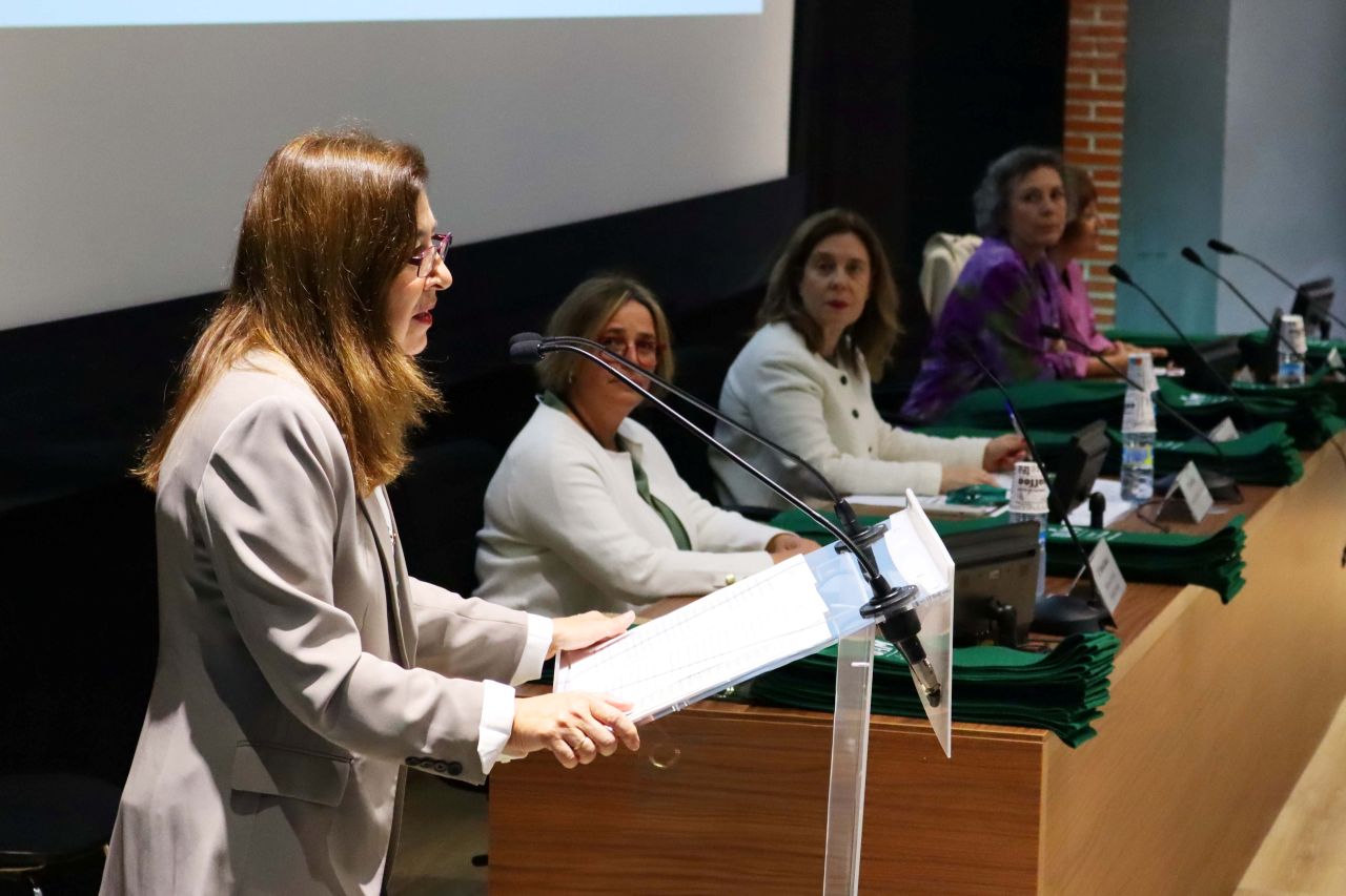 En primer plano, la rectora habla desde el atril. Al fondo, mesa presidencial.