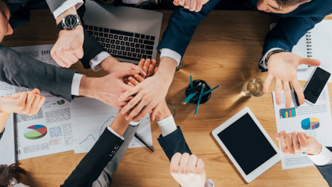 Vista aérea de un equipo de negocios uniendo sus manos sobre una mesa de trabajo con portátiles y gráficos