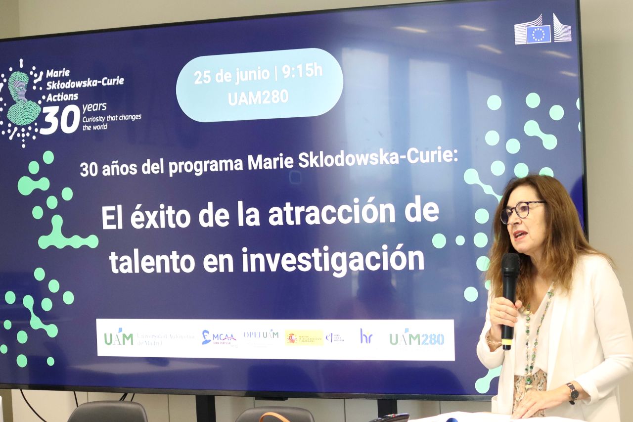 La rectora interviene en el escenario. Al fondo, una pantalla proyecta el título de la jornada